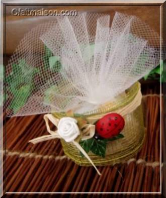Prsentation de drages dans un pot de laitage en verre bas et droit recouvert d'un ruban rustique, finition avec noeud en raphia naturel, lierre, coccinelle et fleurs.