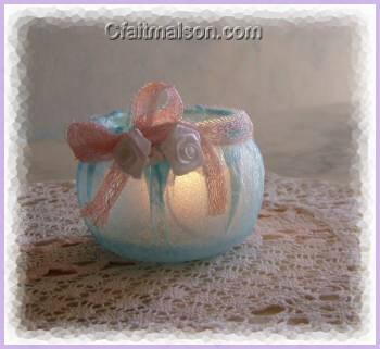 Photophore fait maison avec un pot de laitage en plastique recouvert d'une paisseur de serviette bleue colle, finition avec un noeud rose et de fleurs blanches.